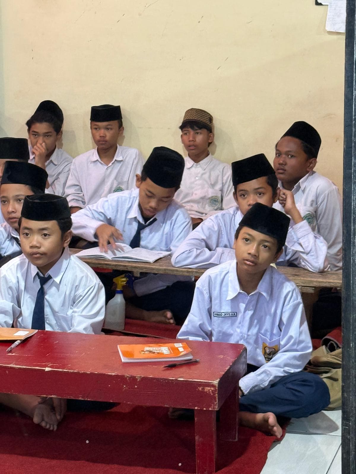 Santri berseragam dan berpeci mengikuti kegiatan belajar di meja kelas
